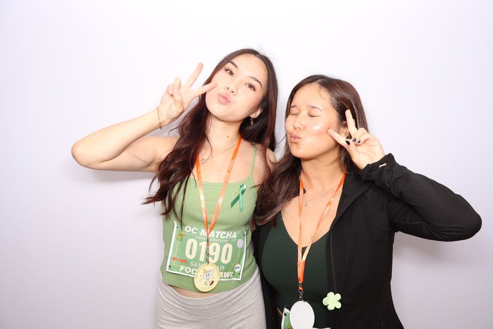 Two friends with race bibs posing in the open-air photo booth