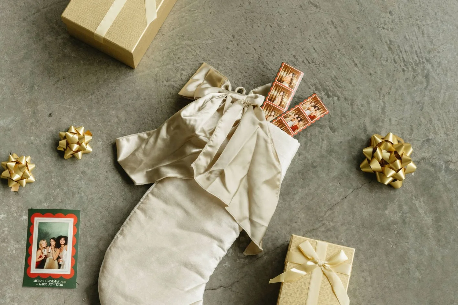 Satin holiday stocking stuffed with photo booth strips beside gold-wrapped gifts