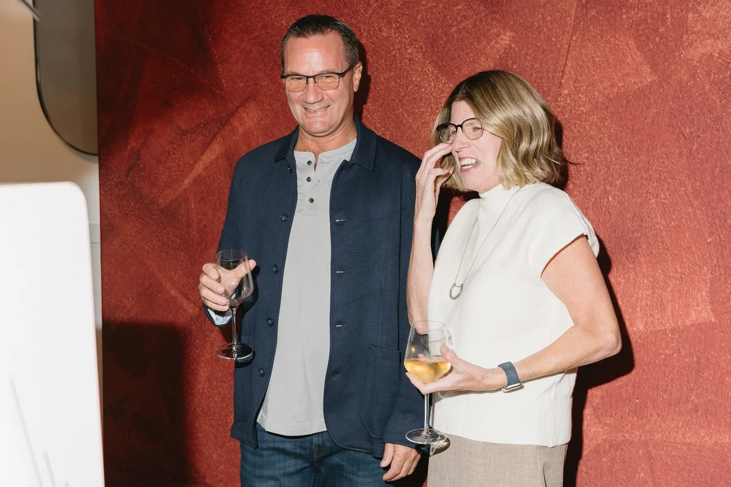 Couple laughing at a photo booth with a terracotta backdrop during a company dinner