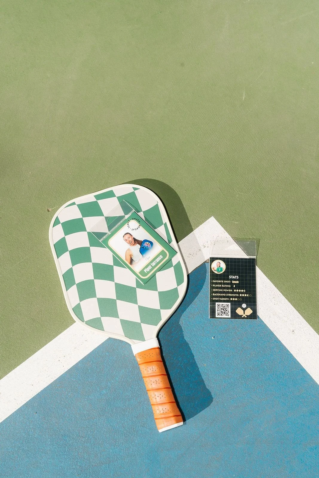 Custom photo trading card resting on a checkered pickleball paddle on court