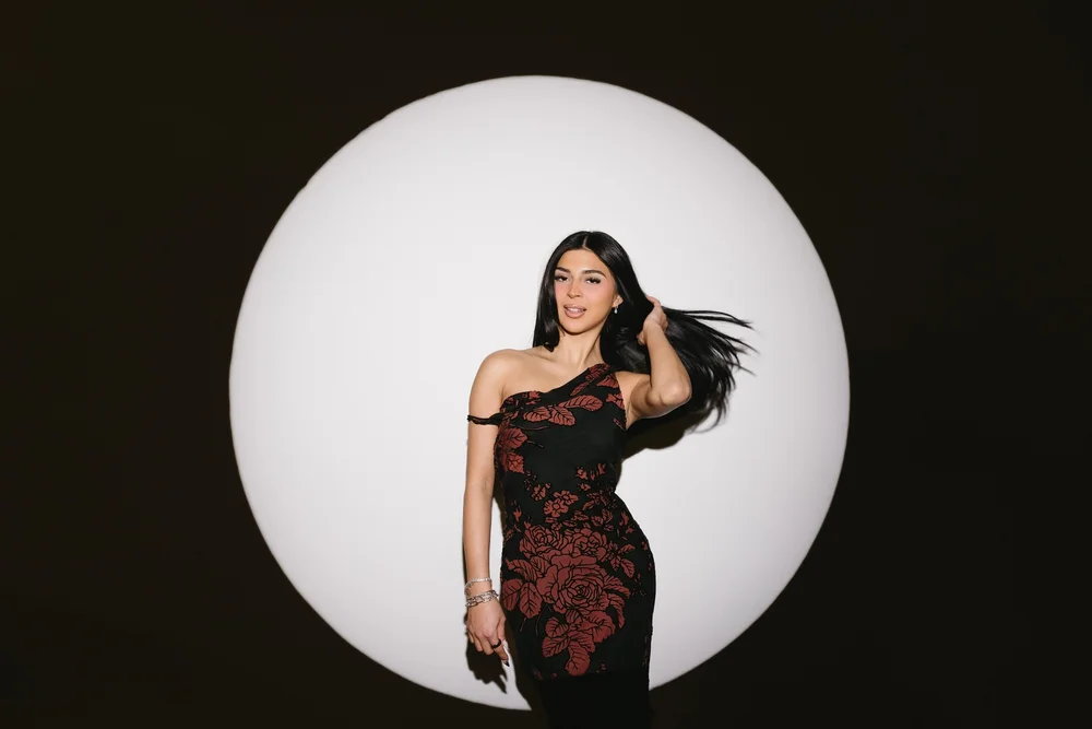 A woman in a black gown turning in a circle of spotlight against a dark wall