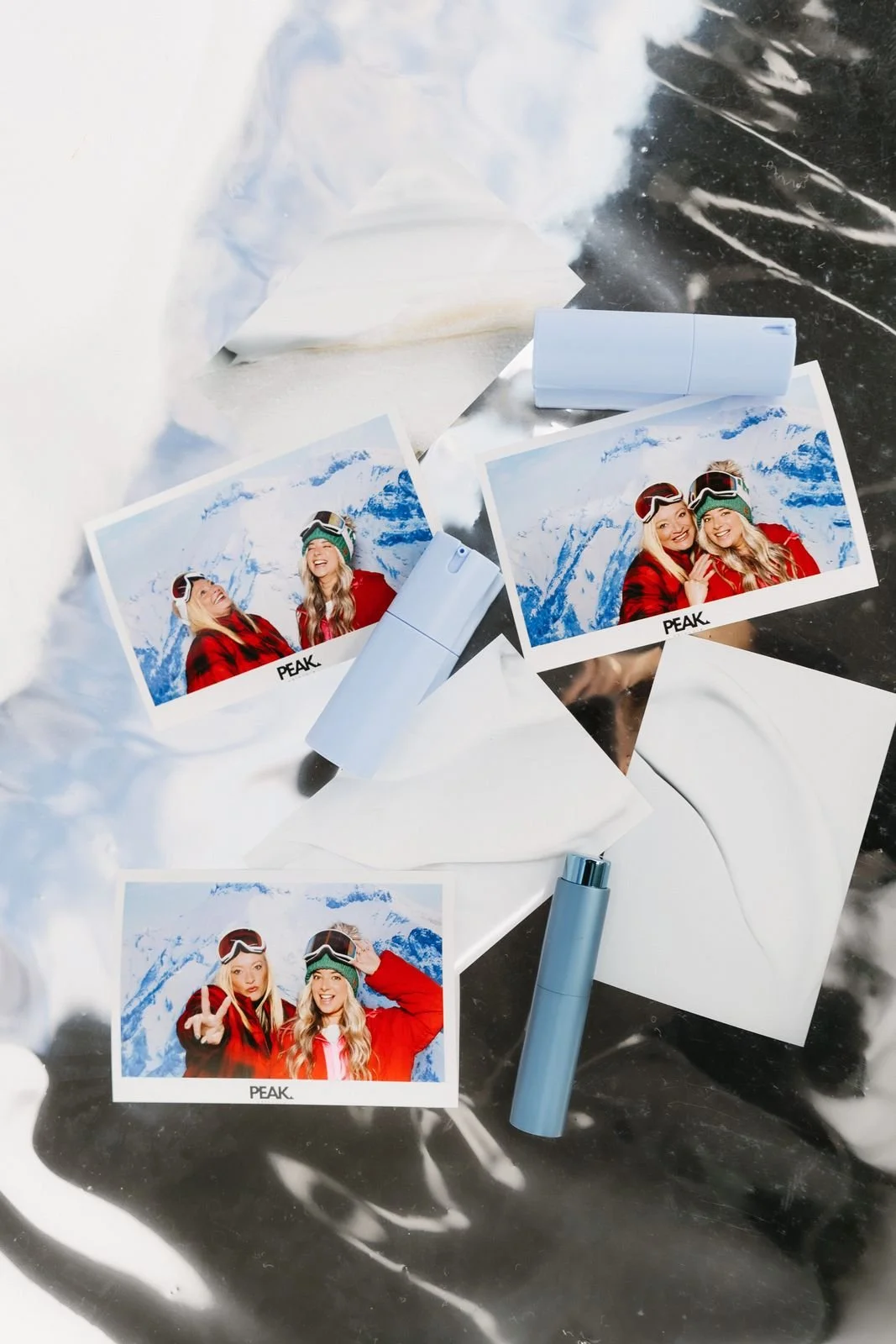 Holiday photo booth prints of friends in ski jackets laid out on a glossy winter-white surface
