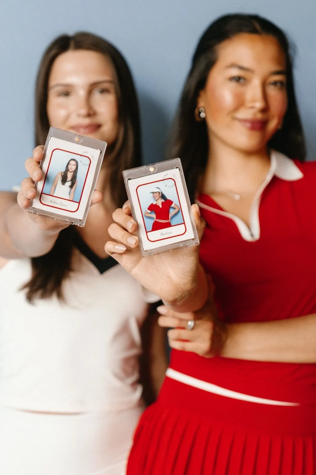 Two guests in tennis whites holding up their cased custom photo trading cards