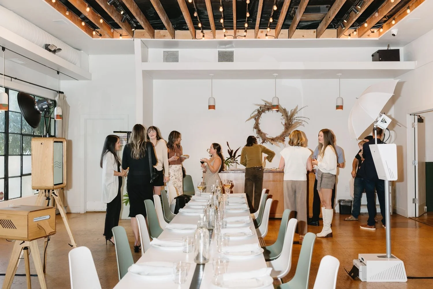 Company dinner in a bright loft with long white tables and a photo booth set up beside the guests