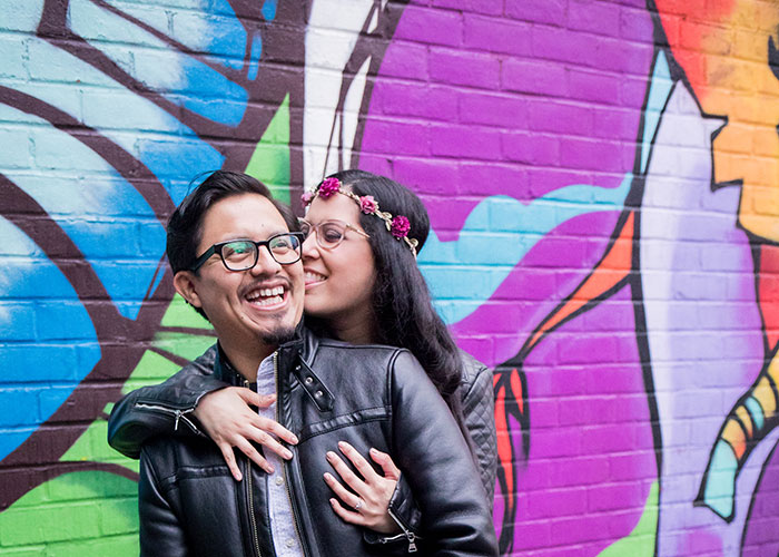 engaged couple embraced in front of mural wall