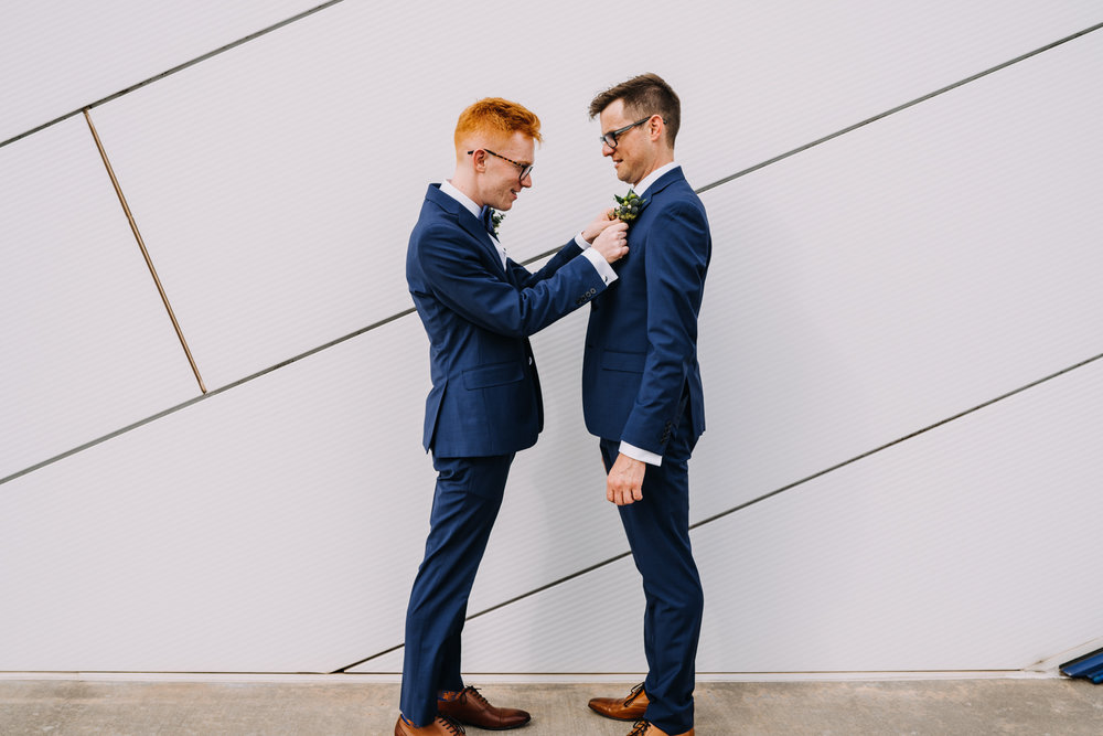 two grooms in blue suits one putting boutonniere on the other