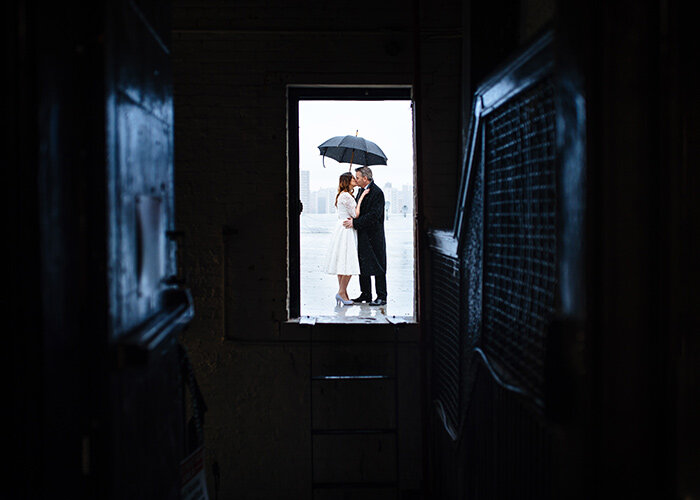 newlyweds kiss on NYC rooftop under umbrella during rain after wedding JC Lemon Photography
