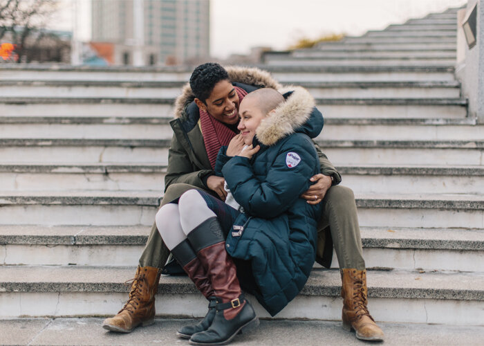 couple snuggles together in winter coats on outdoor steps during engagement session Shannon Collins Photo