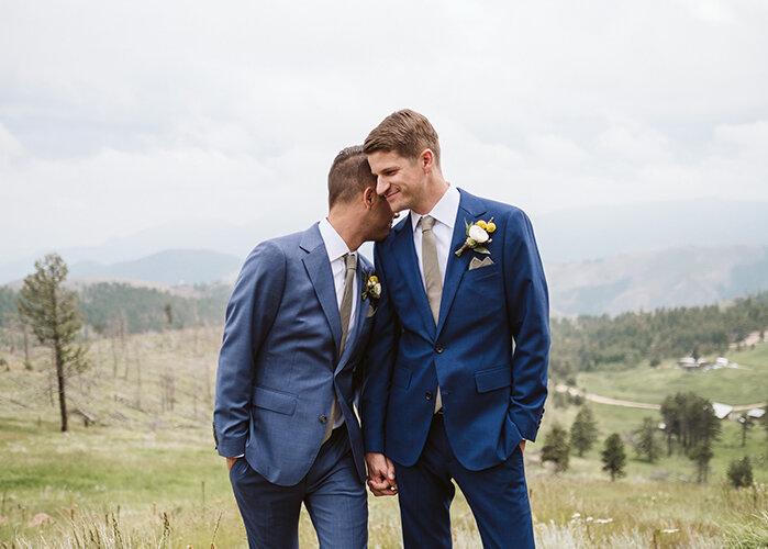 newlywed grooms hold hands in matching suits in open field Larsen Photo Co Colorado