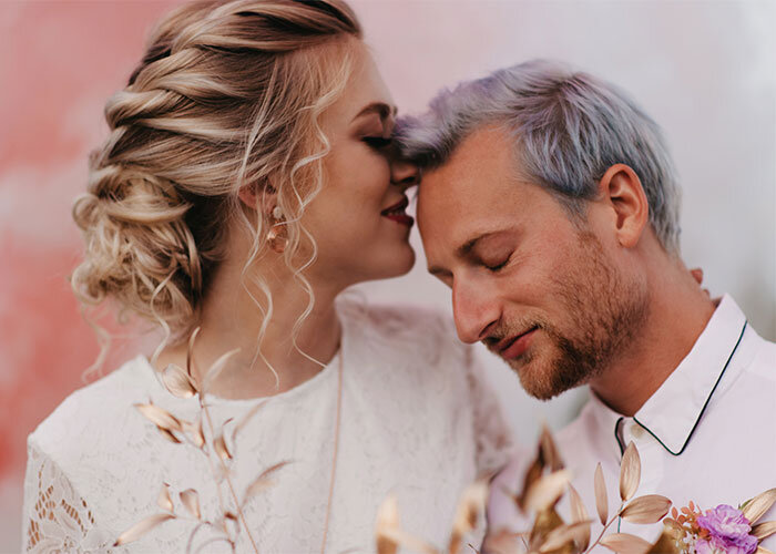 Newlyweds embrace against pink smoky background The Stylist Abroad Wedding Beauty