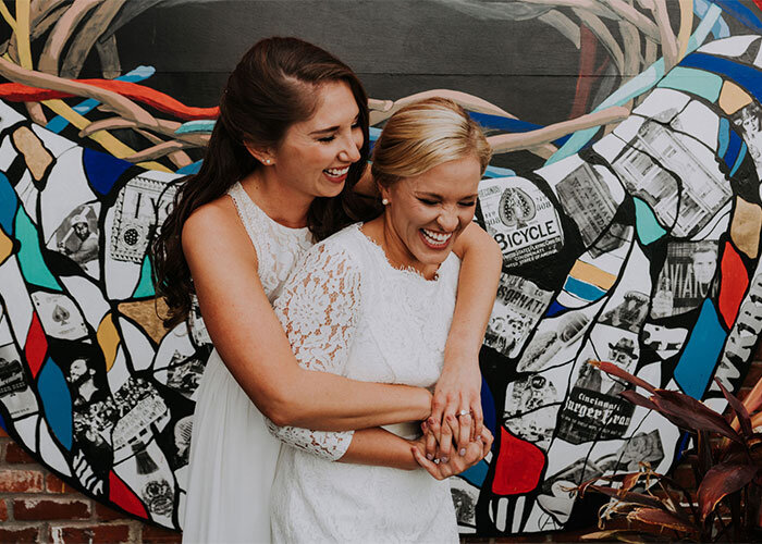 Newlywed brides embrace in front of mural wall De Evans Events Cincinnati Ohio