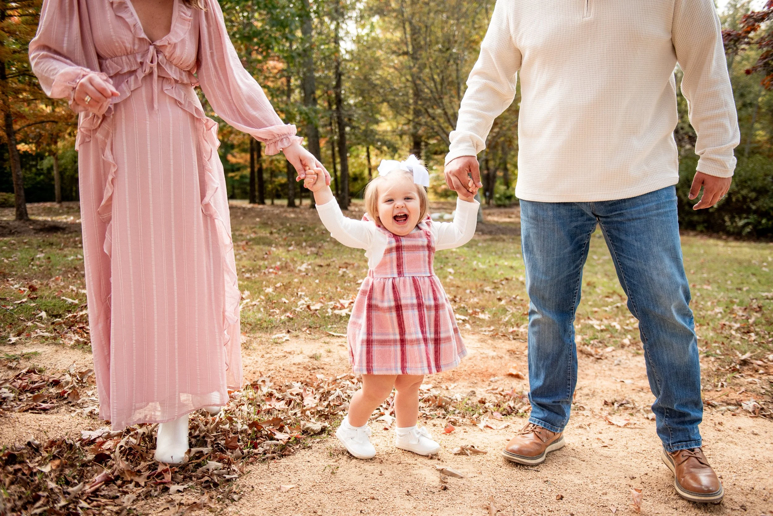 Toddler holding her parents' hands on a fall walk in Burlington, NC
