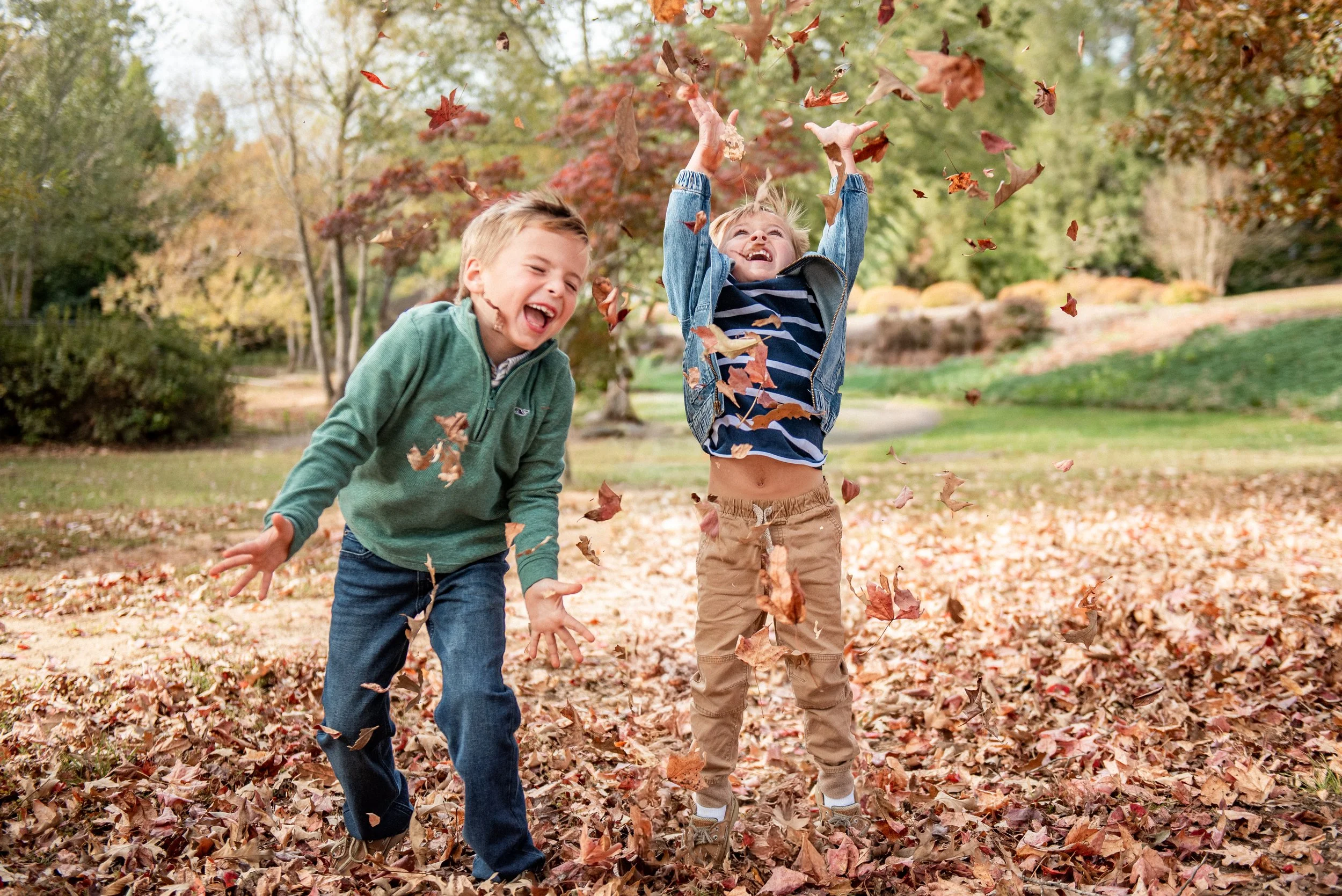Two brothers laughing and throwing fall leaves during a Burlington, NC mini session