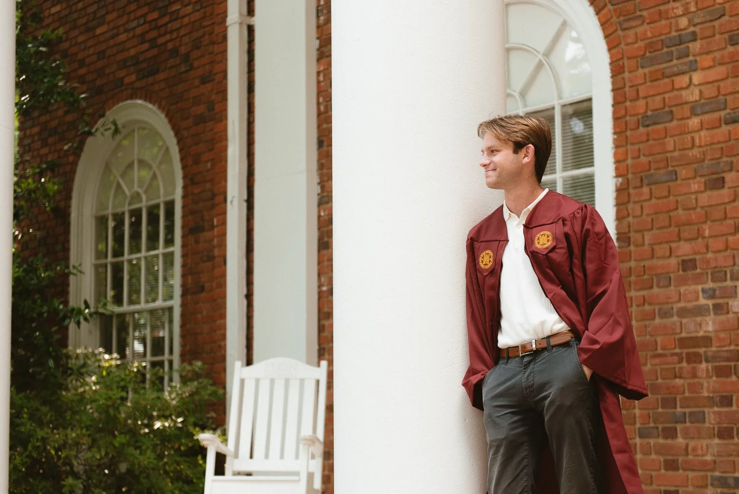 Elon graduate leaning against a white column beside arched windows