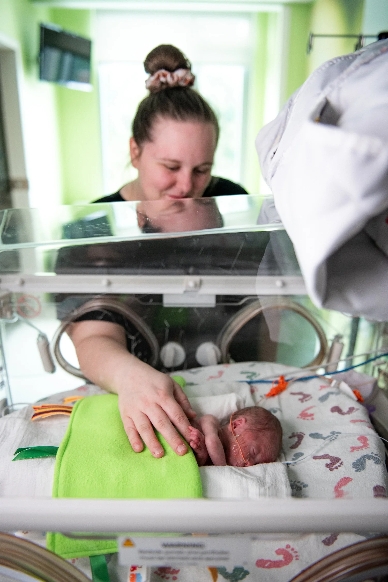A mother watches over her baby in a NICU isolette