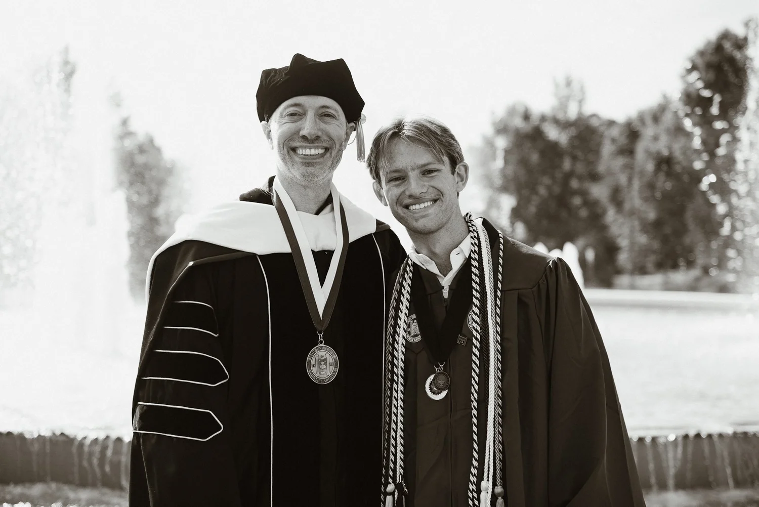 Black and white photograph of an Elon graduate with his professor in academic regalia at the fountain