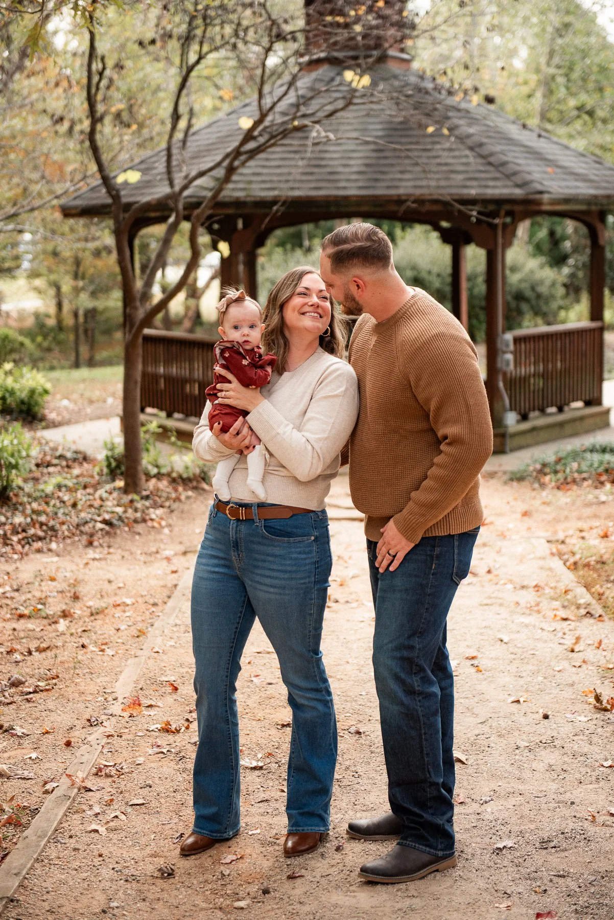 Family of three smiling together at a fall gazebo in Burlington, NC