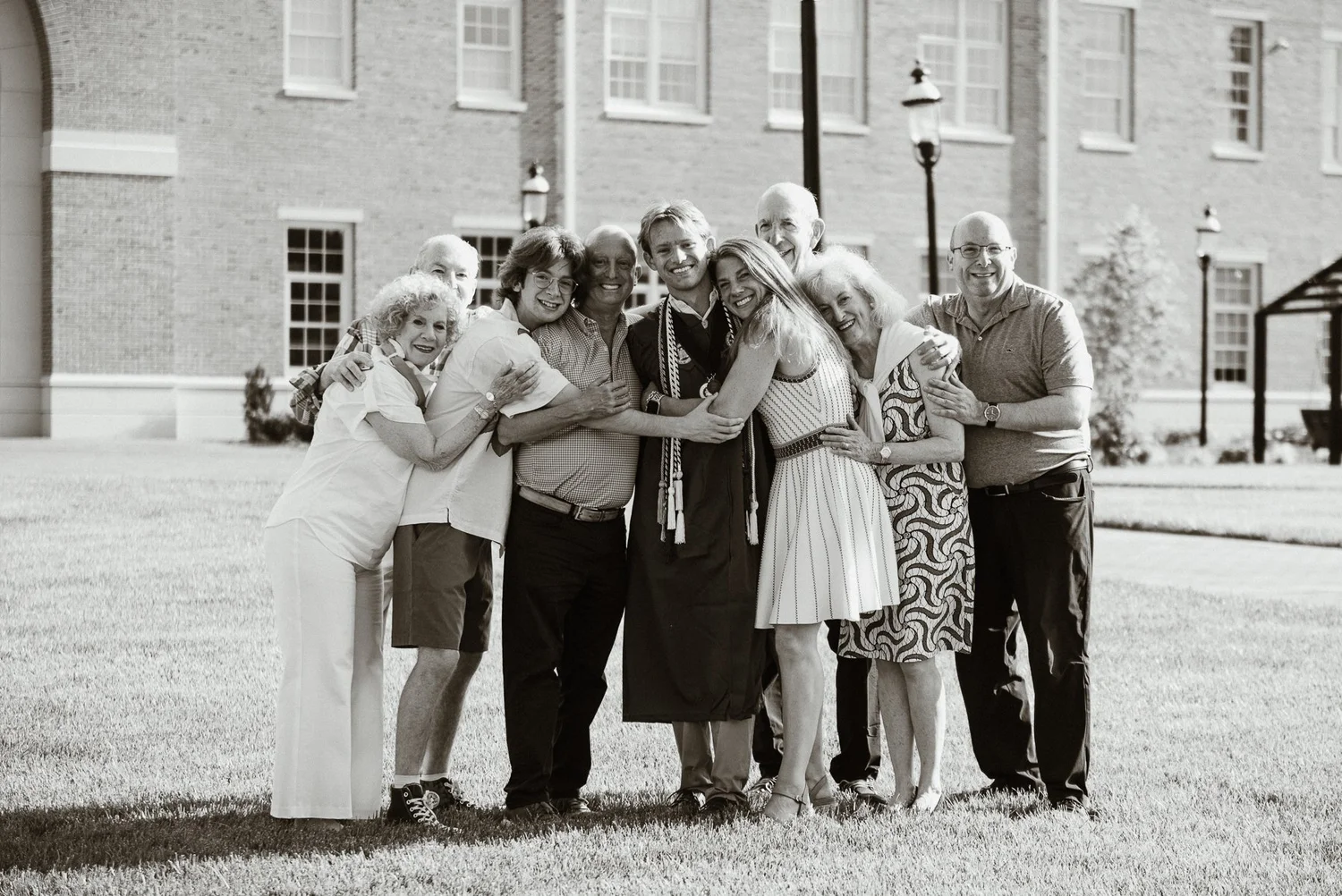 Black and white photograph of an Elon graduate hugging his extended family on campus