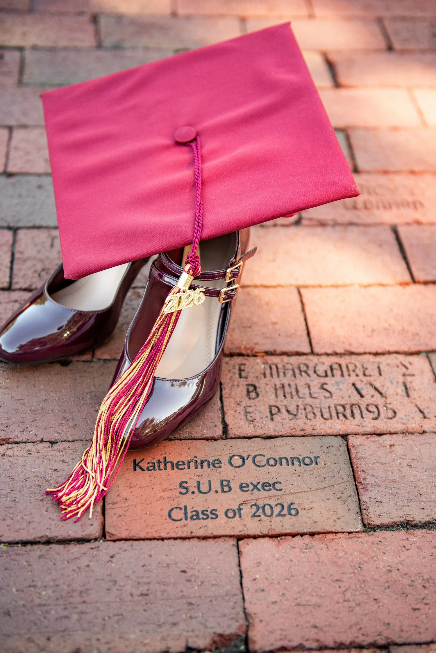 Maroon graduation cap and heels resting on an engraved Elon brick