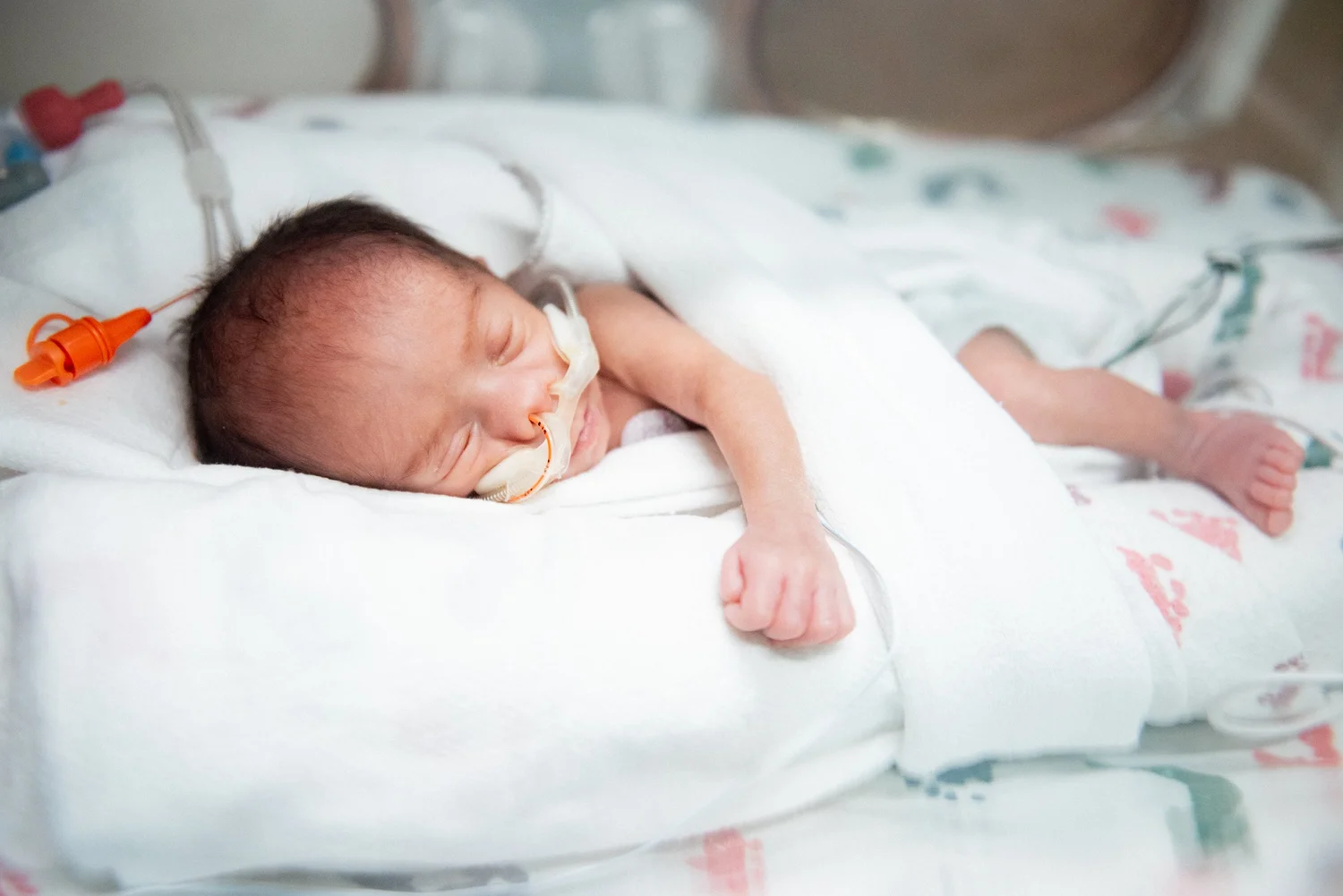 A sleeping baby tucked in a white blanket in the NICU