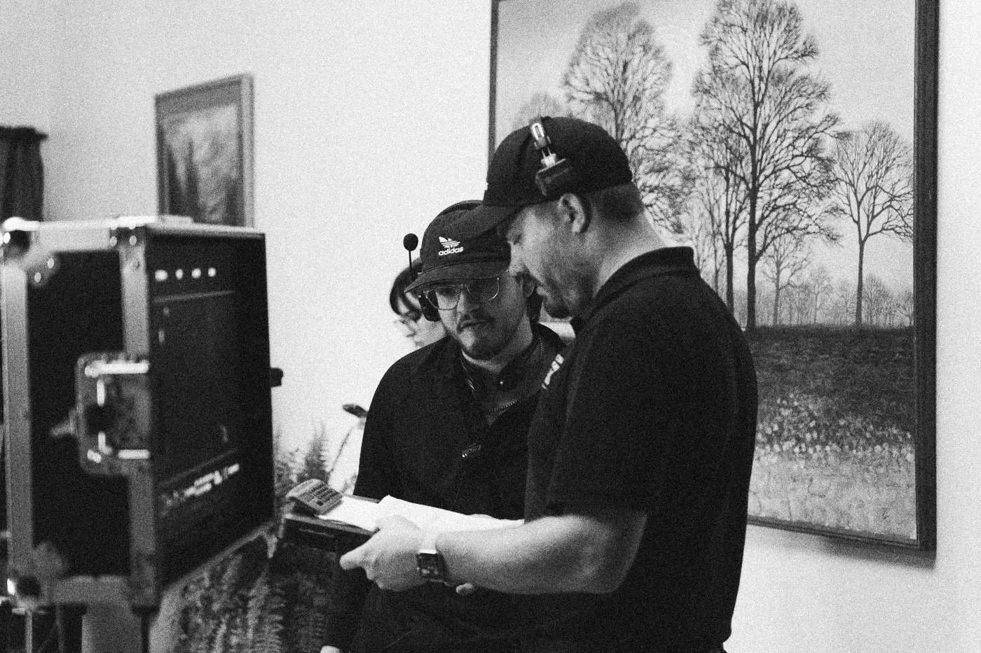 Behind the scenes on INERTIA: two crew members in caps watch a field monitor.