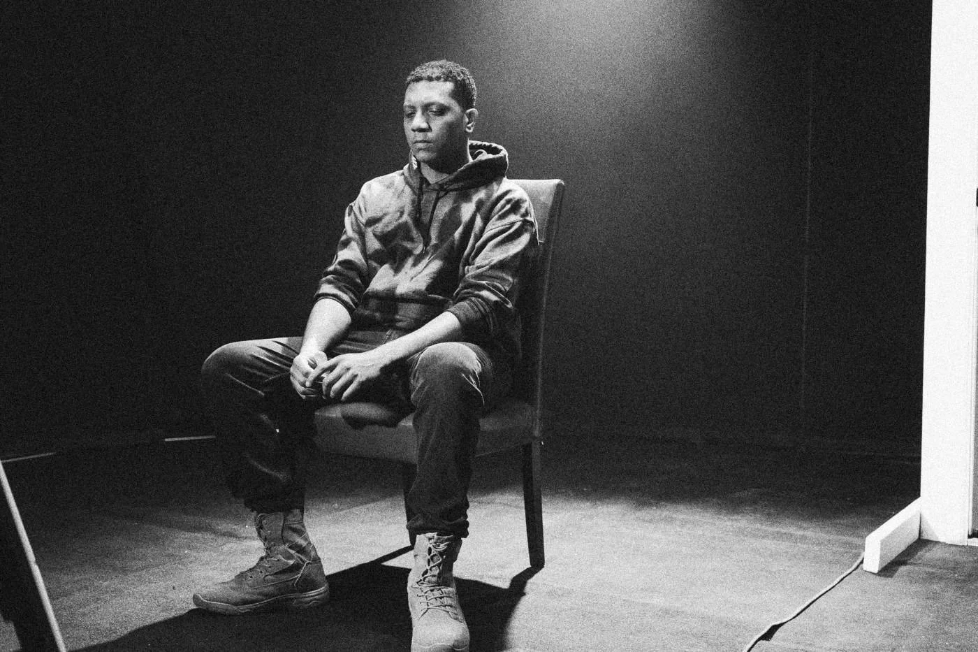 Behind the scenes on INERTIA: an actor sits on a red chair in a dark studio under a spotlight, looking toward the camera.