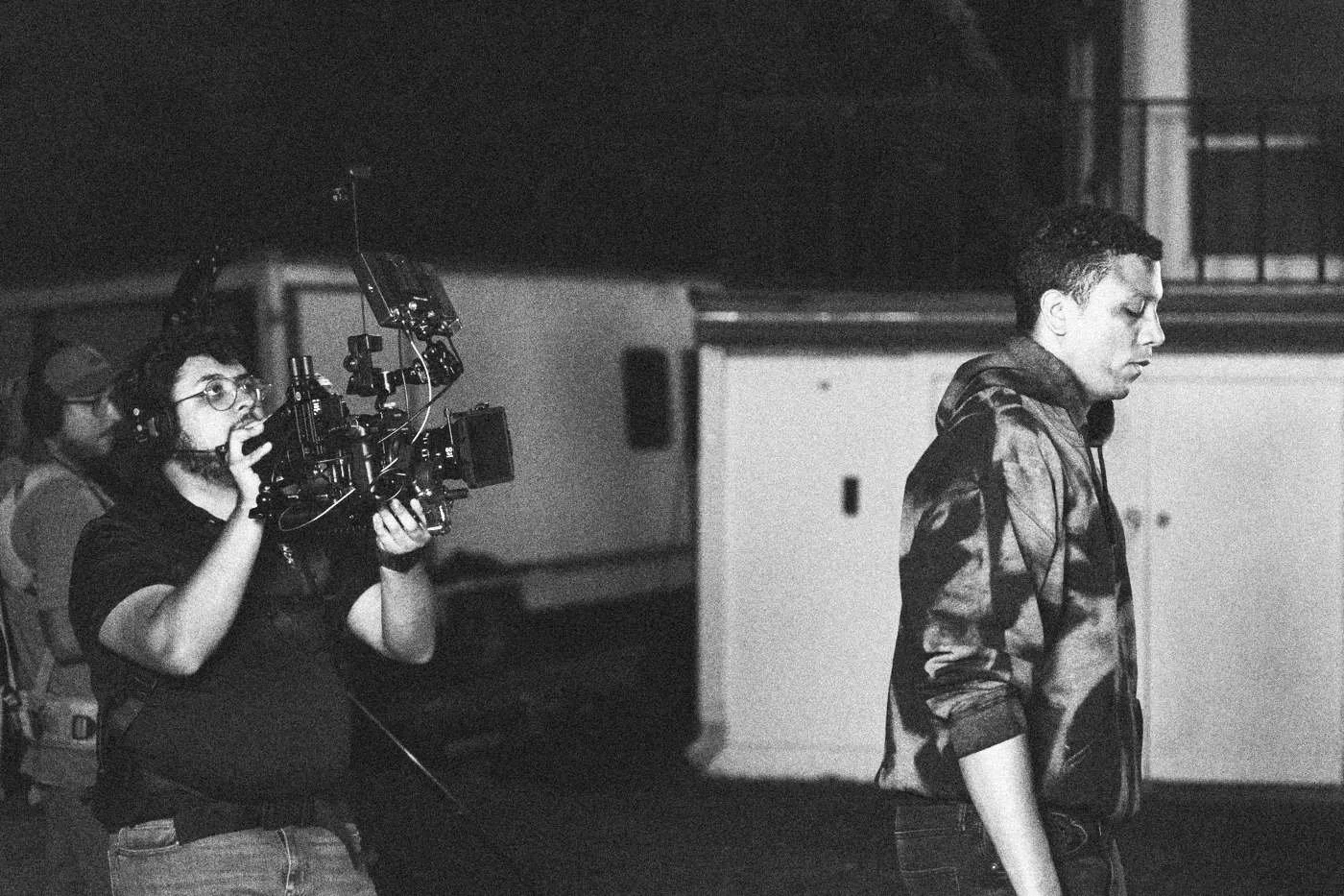 Behind the scenes on INERTIA: a camera operator films an actor standing outside a trailer at dusk.