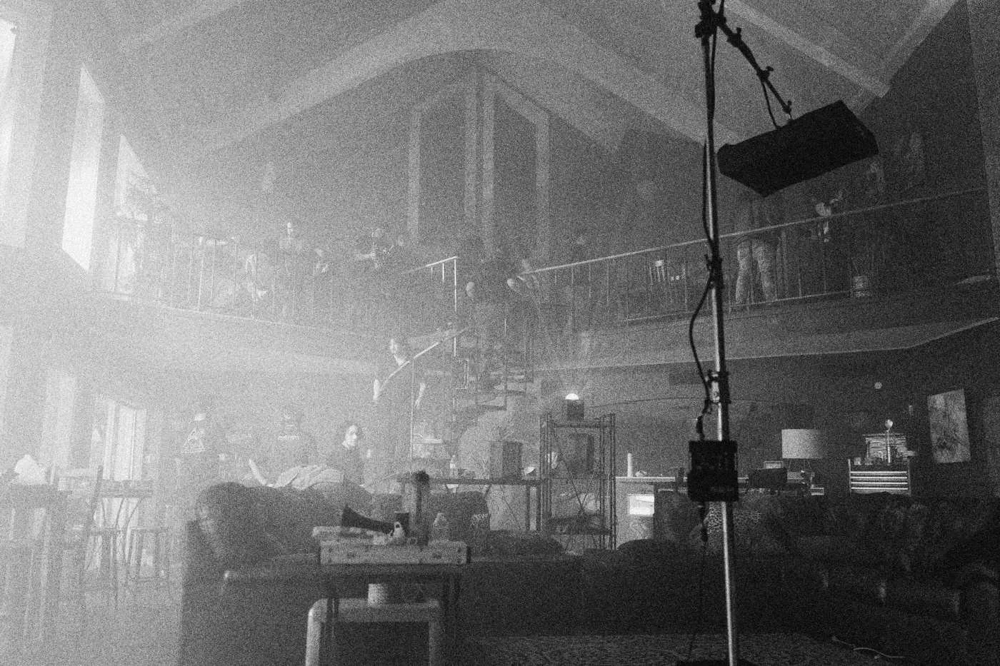 Behind the scenes on INERTIA: wide view of a hazy two level room with a light stand in the foreground and balconies behind.