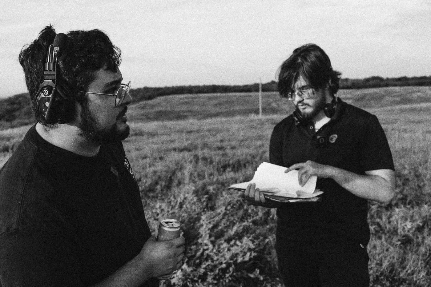 Behind the scenes on INERTIA: two crew members read script pages in a grassy field.