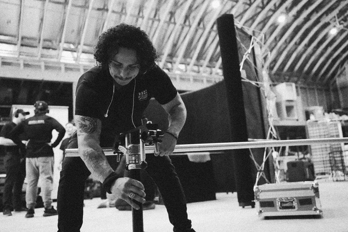 Behind the scenes on INERTIA: a crew member smiles while adjusting a camera on a slider in a warehouse studio.