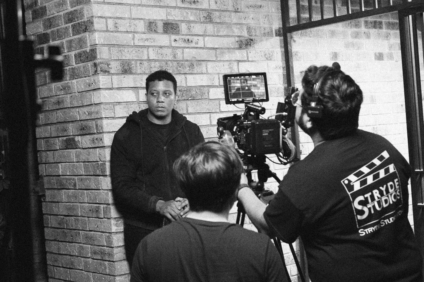 Behind the scenes on INERTIA: the camera team films an actor standing against a brick wall at night.
