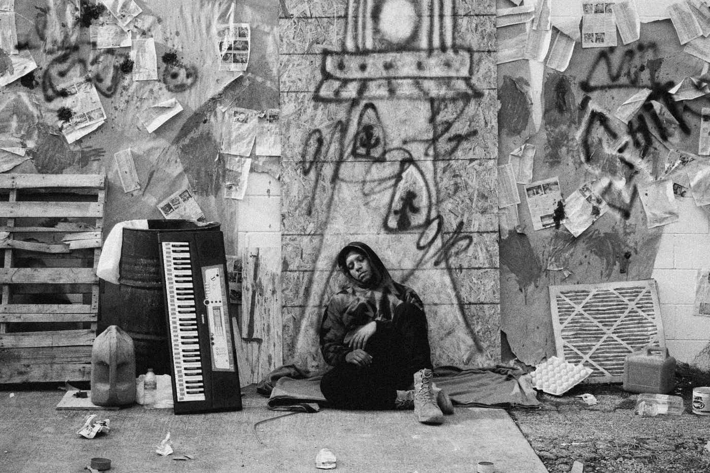 Behind the scenes on INERTIA: an actor slumps against the graffiti set wall with his hood up.
