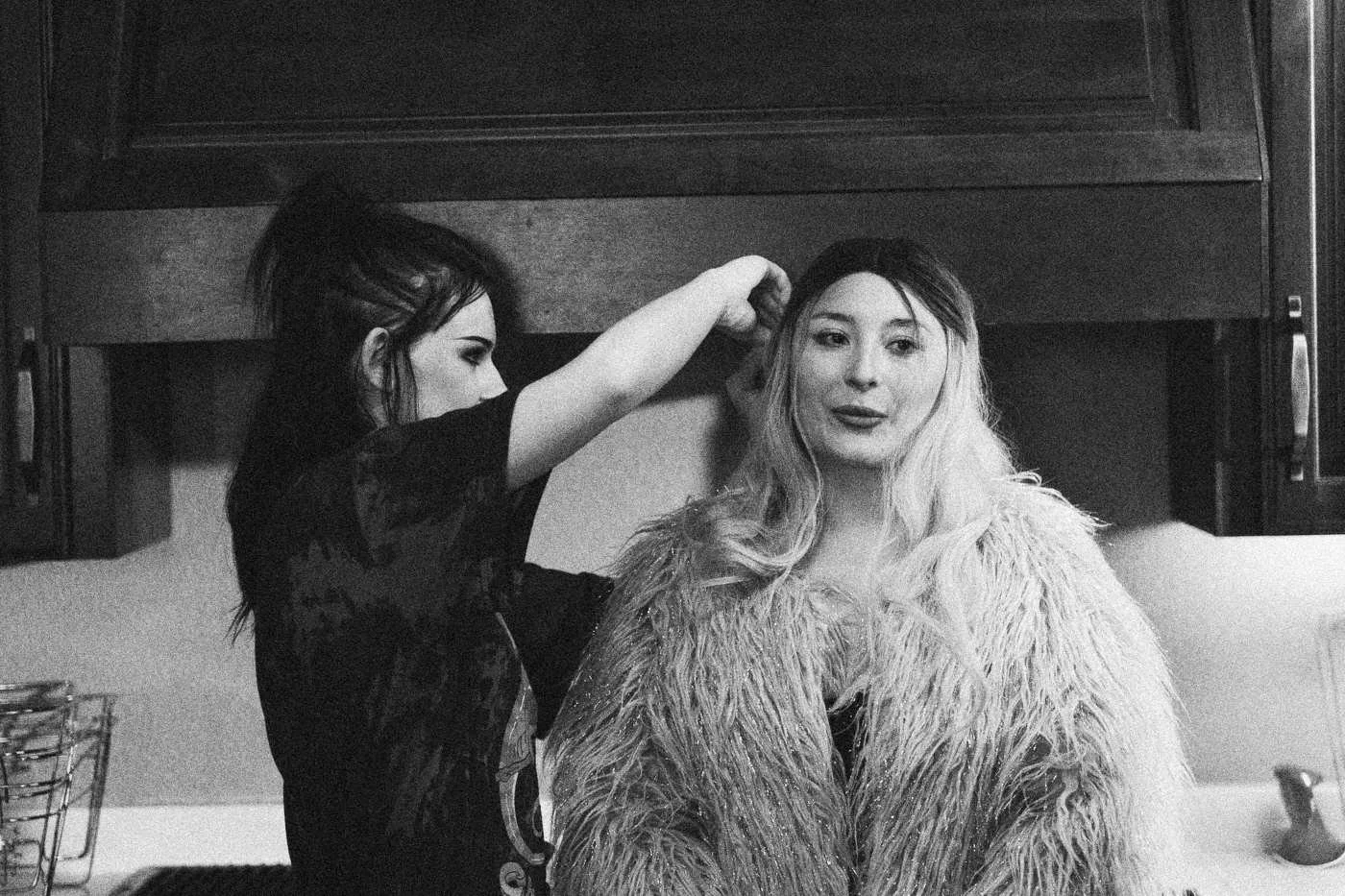 Behind the scenes on INERTIA: a makeup artist adjusts the hair of an actress in a pink faux fur coat.