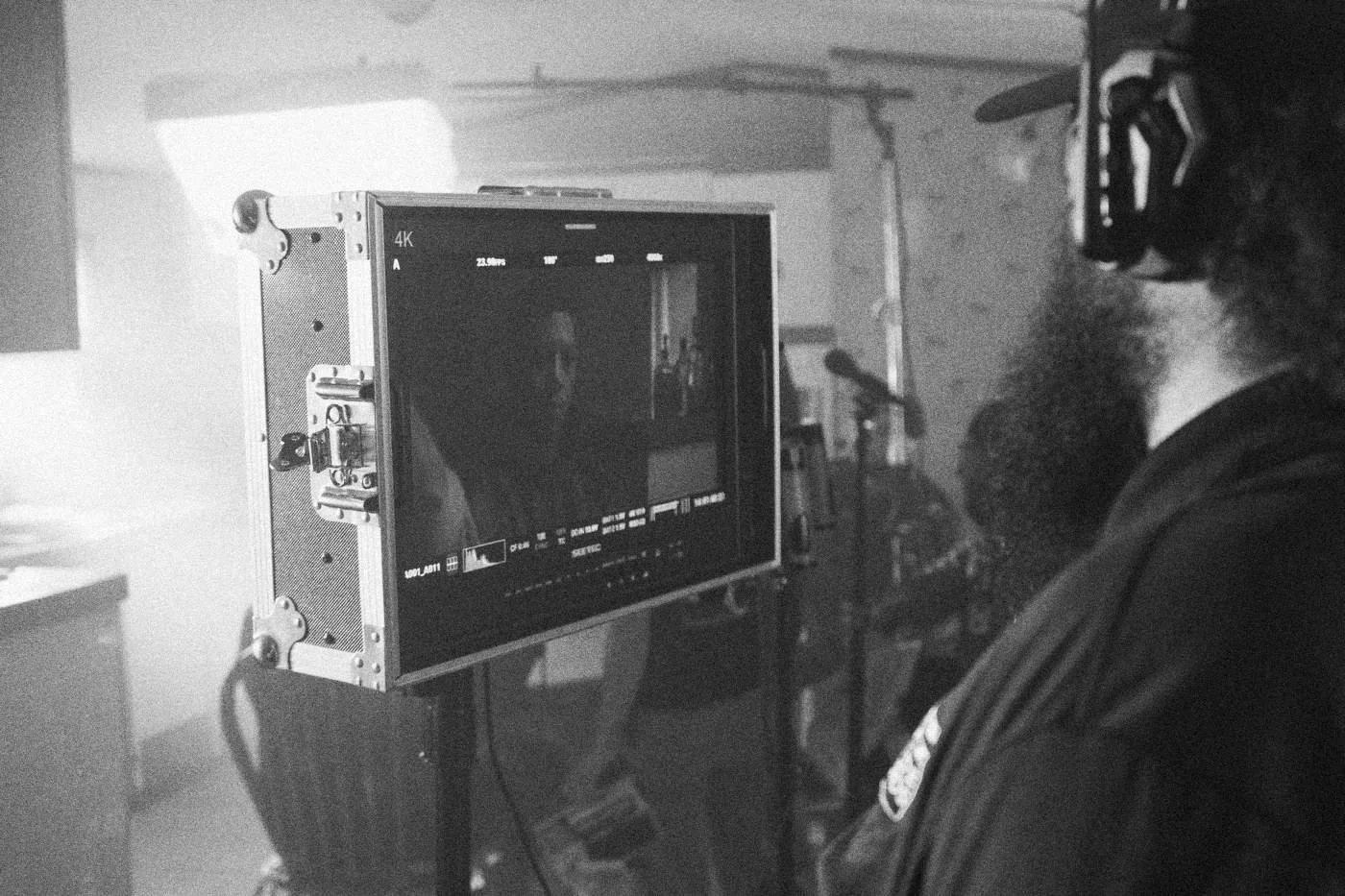 Behind the scenes on INERTIA: a monitor shows an actress in close up while crew members stand beside it in hazy light.