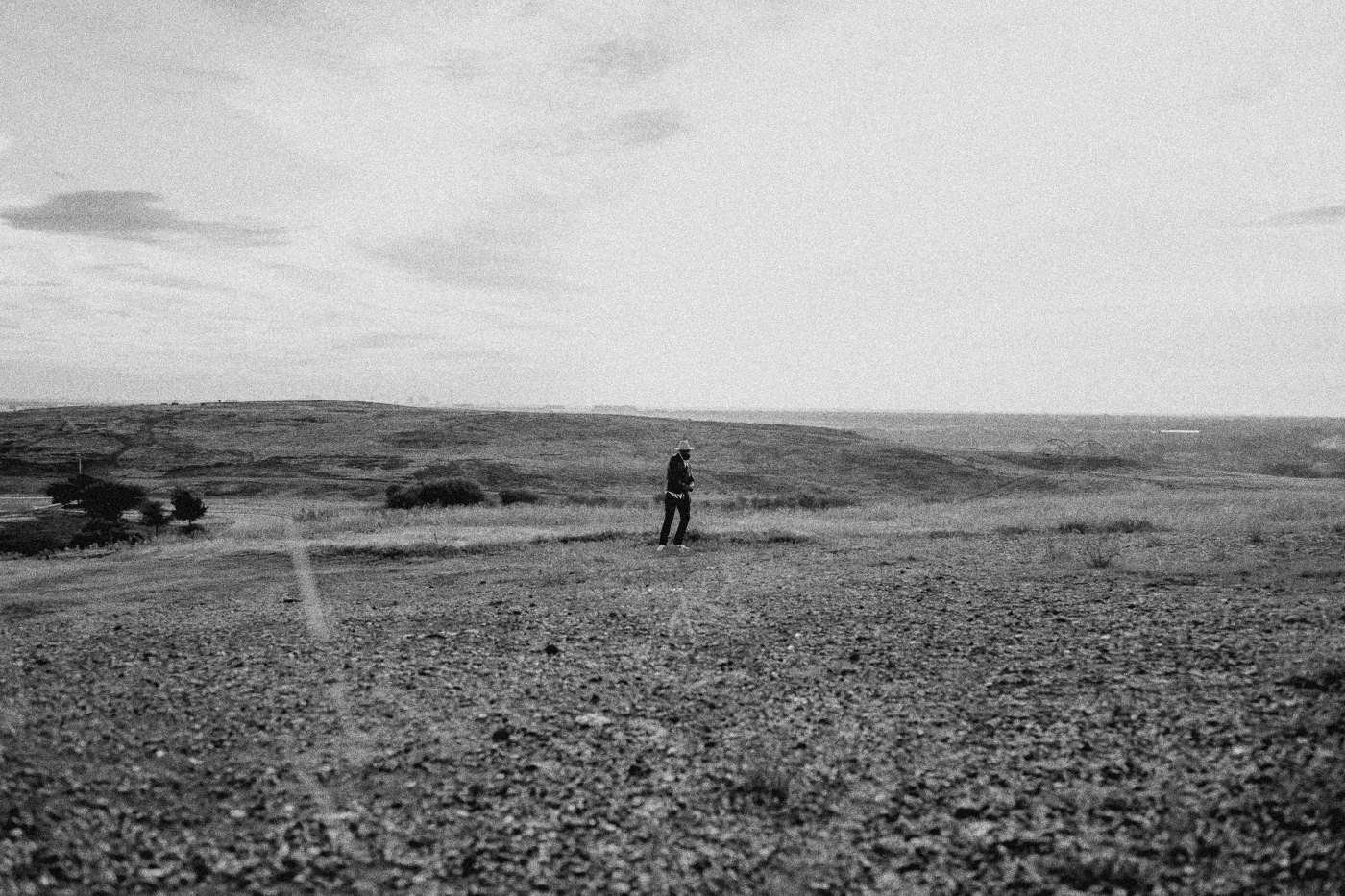 Behind the scenes on INERTIA: a wide empty gravel hilltop at dusk with one small figure in the distance.