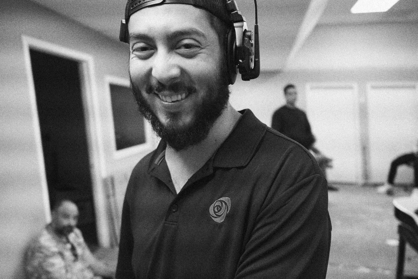 Behind the scenes on INERTIA: a smiling crew member in a headset looks at the camera in a rehearsal room.
