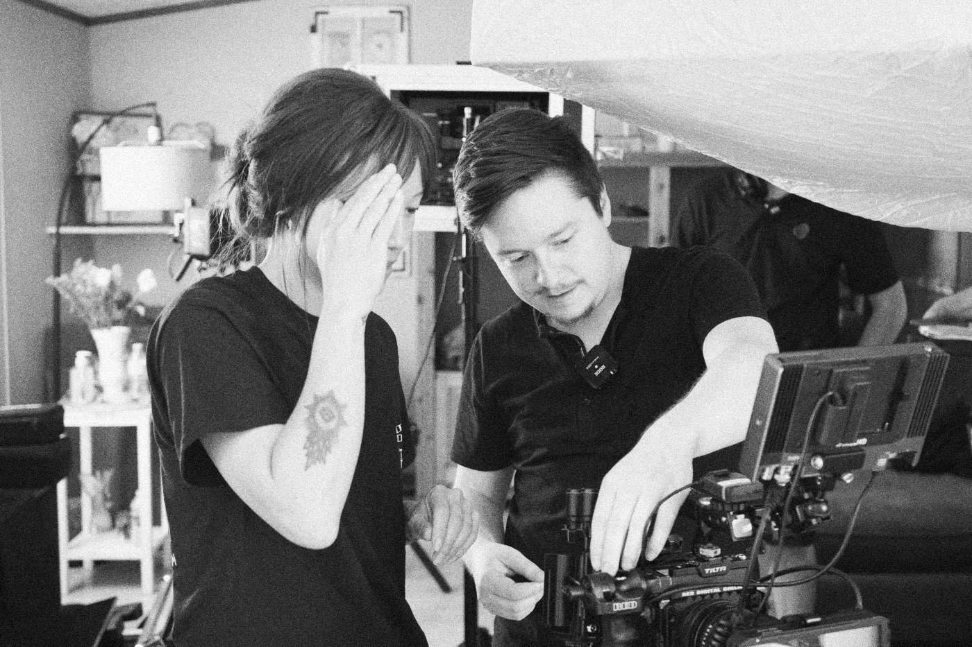 Behind the scenes on INERTIA: a crew member covers her face with her hand while a colleague adjusts a camera rig in a kitchen.