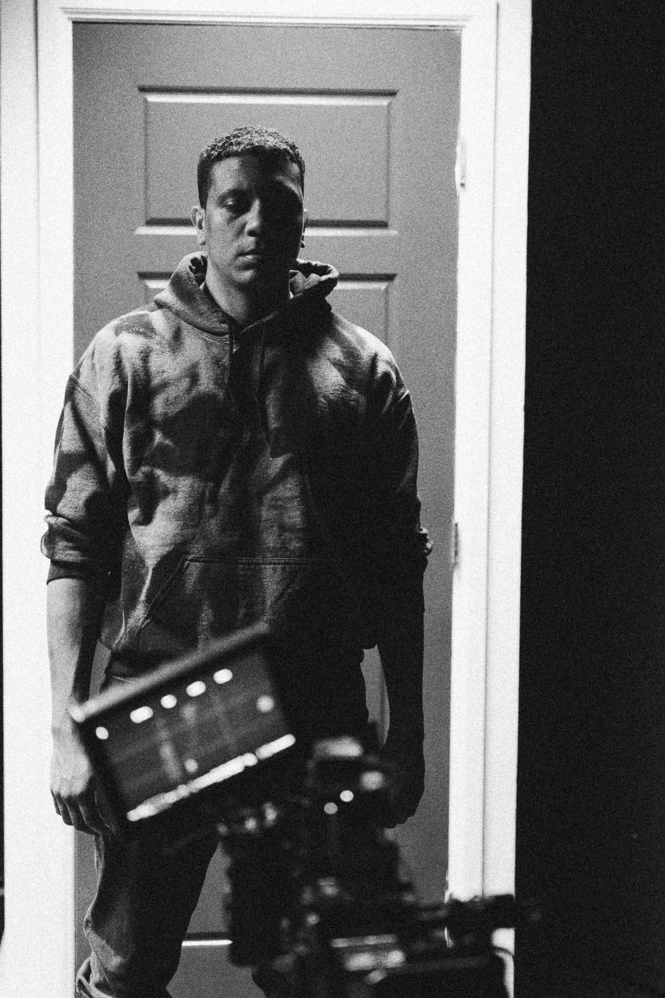 Behind the scenes on INERTIA: an actor in a camouflage hoodie standing before a red door, a camera in the foreground.