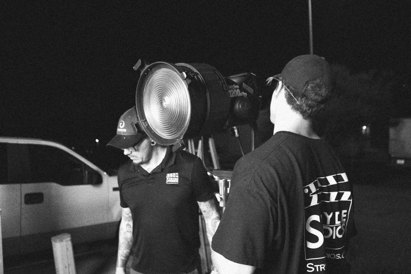 Behind the scenes on INERTIA: two crew members set a large fresnel light beside a pickup truck at night.