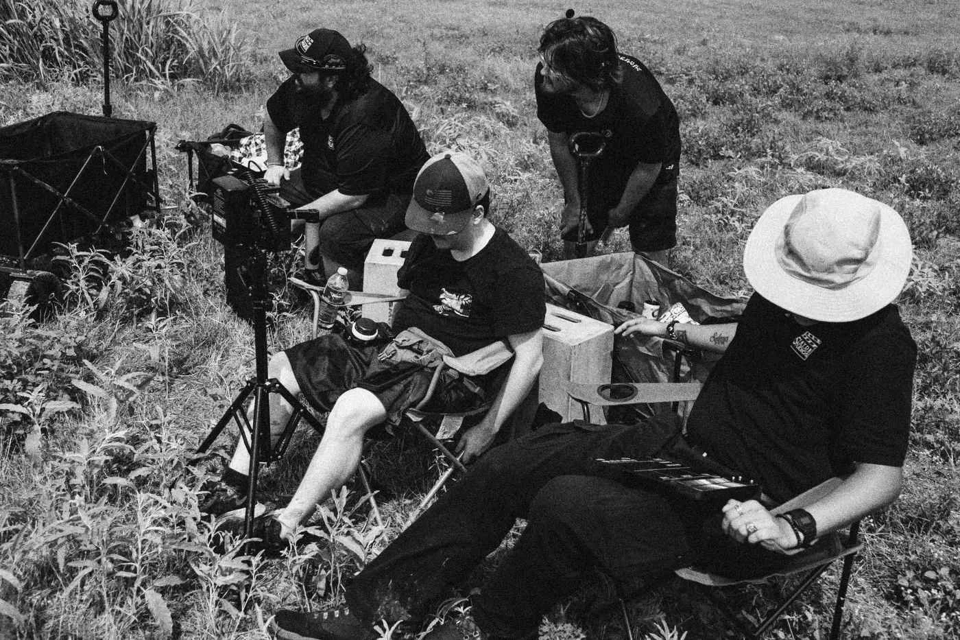 Behind the scenes on INERTIA: crew members rest in camping chairs among gear in tall grass.