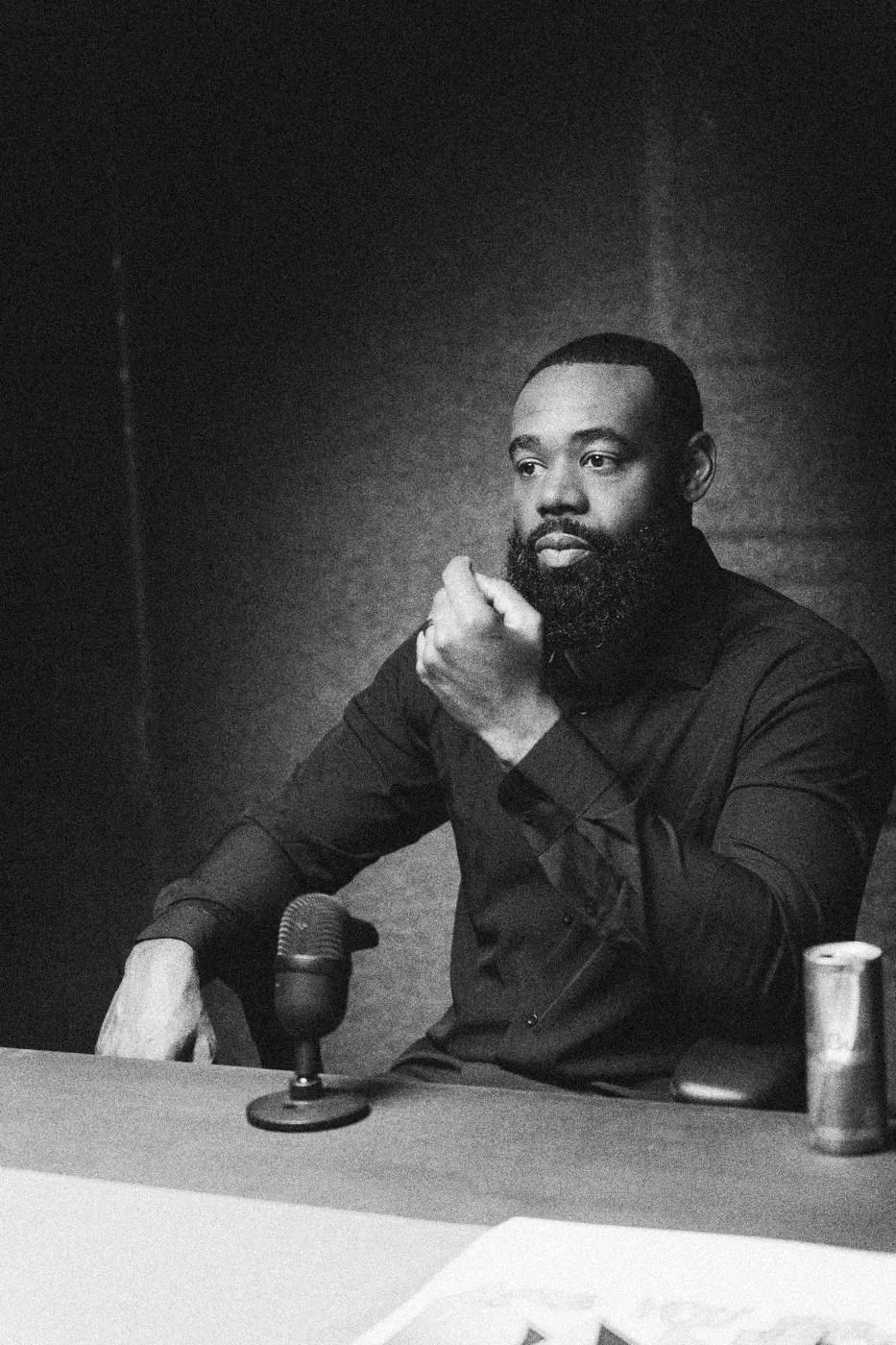 Behind the scenes on INERTIA: an actor seated at a table under an overhead light, fist at his chin.