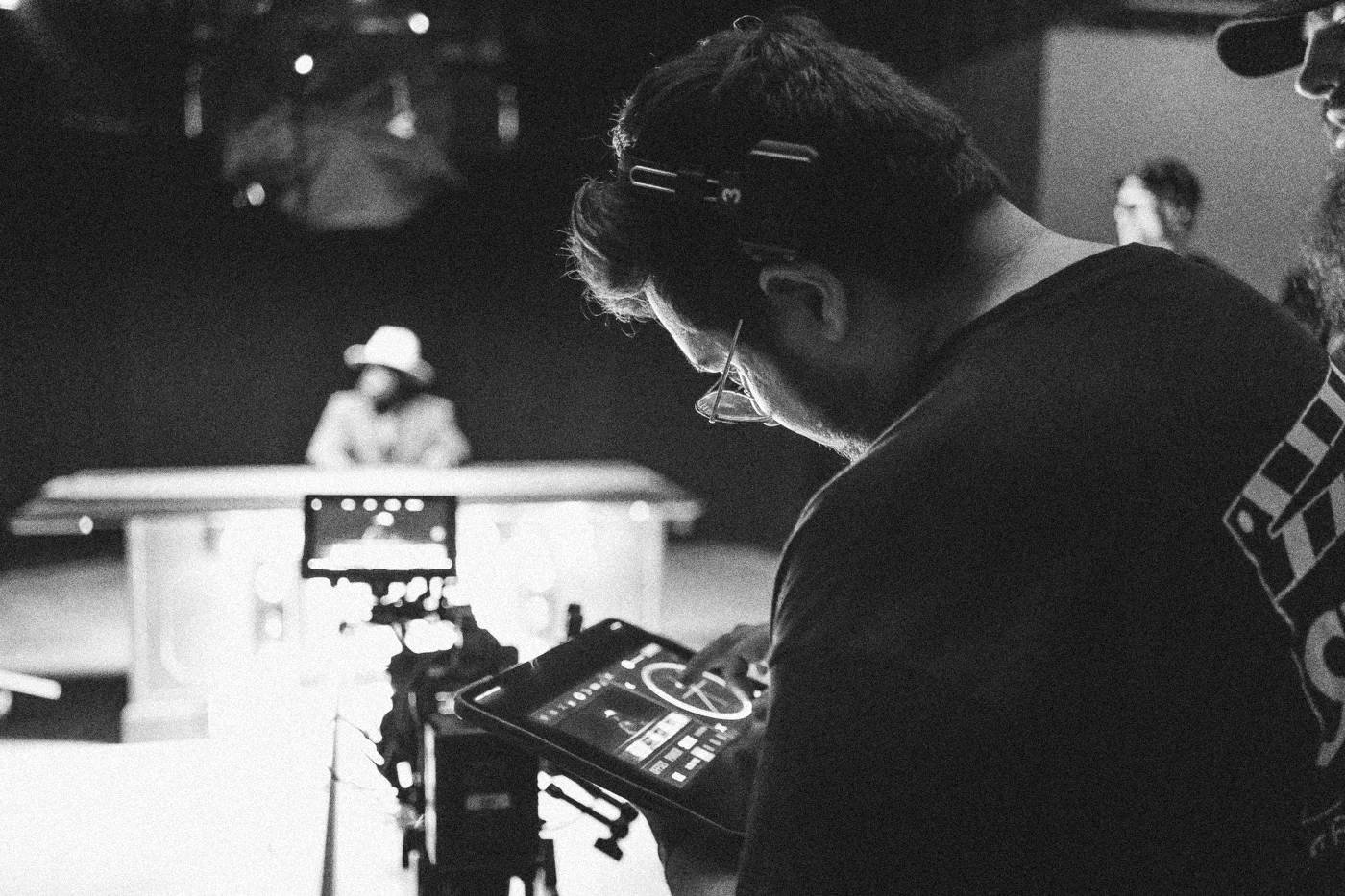 Behind the scenes on INERTIA: a crew member checks a tablet over the camera while an actor waits at a lit game show desk.