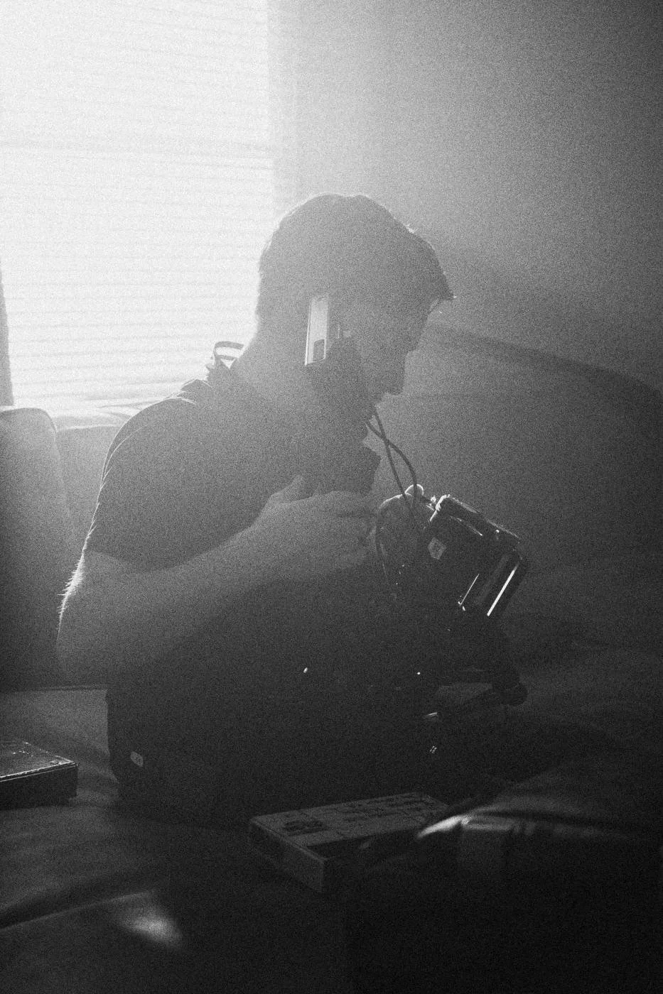 Behind the scenes on INERTIA: a camera operator in soft haze, backlit by a window.