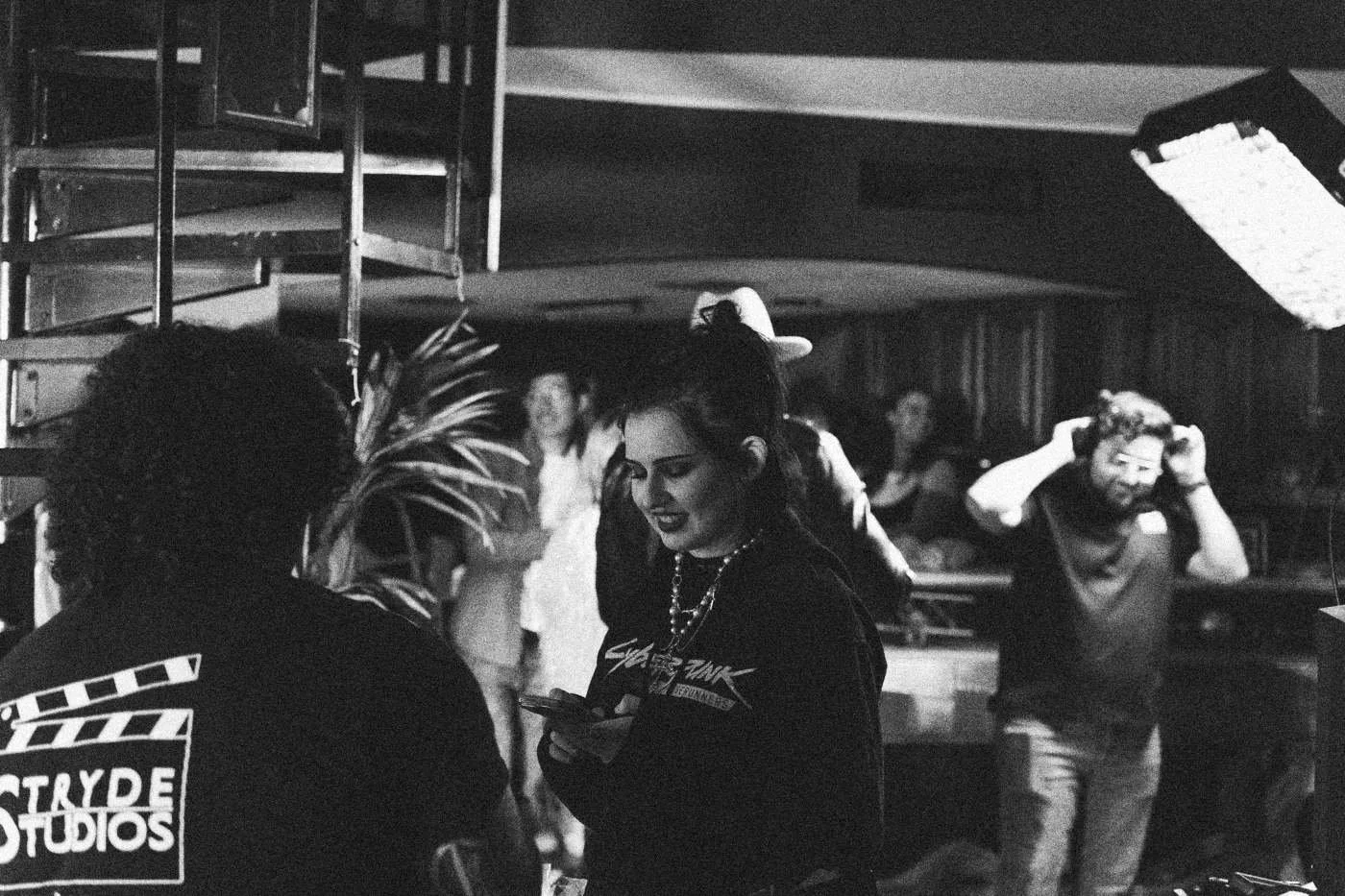 Behind the scenes on INERTIA: crew members in slate branded shirts work around a busy party set.