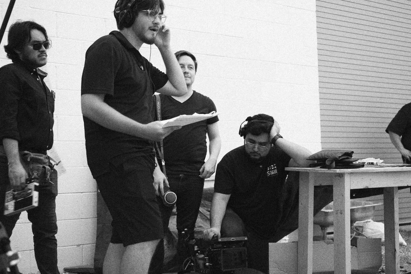 Behind the scenes on INERTIA: crew members stand by a white wall going over pages, one holding a slate.