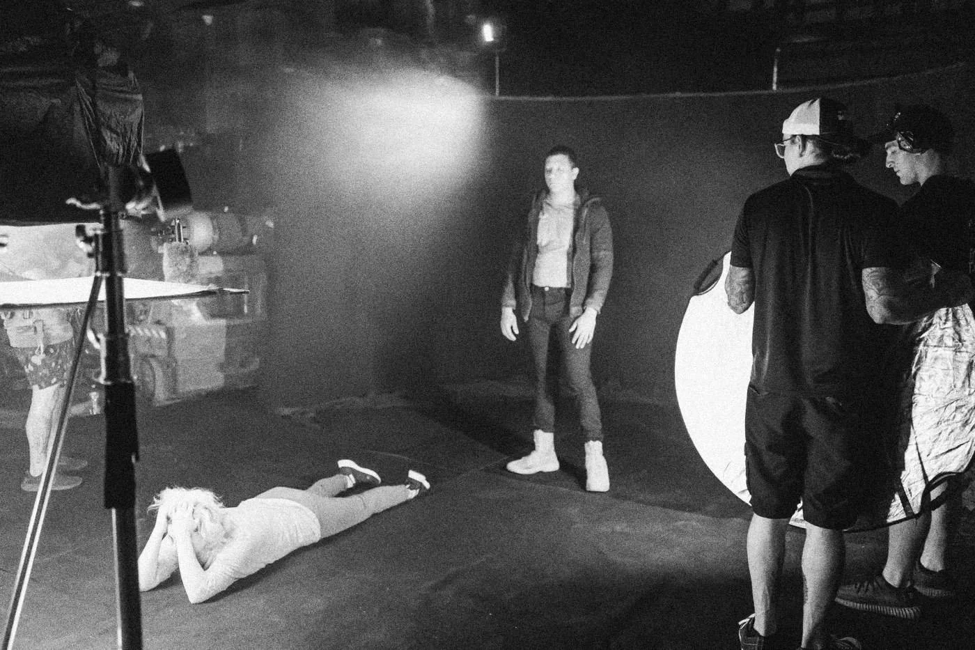 Behind the scenes on INERTIA: an actress stands on a dark set while another lies on the floor and crew hold a reflector.