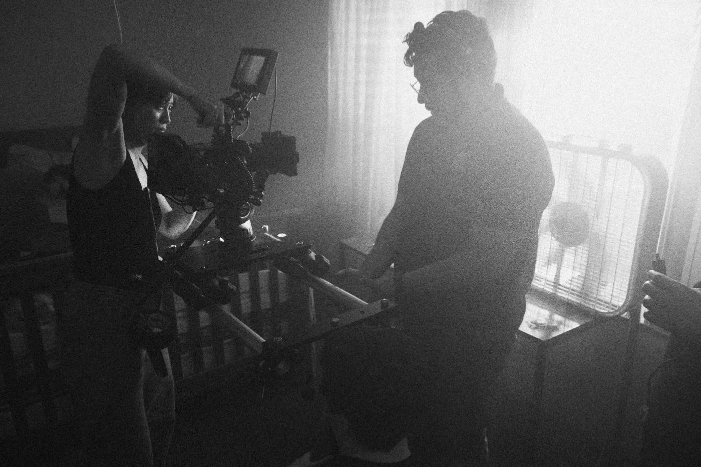 Behind the scenes on INERTIA: a camera operator and a crew member work a rigged camera in a backlit room.
