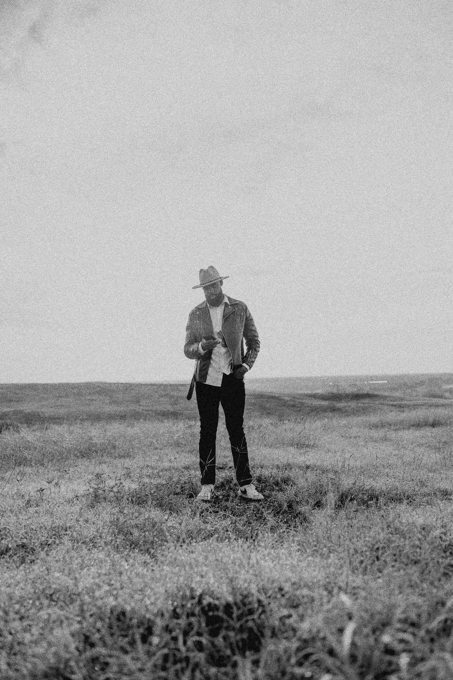Behind the scenes on INERTIA: a lone man in a hat standing in tall grass under a white sky.
