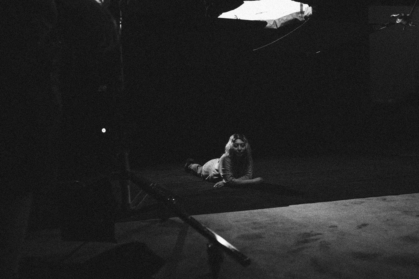 Behind the scenes on INERTIA: a dark studio floor with one small pool of light on an actress lying down, the rest in shadow.