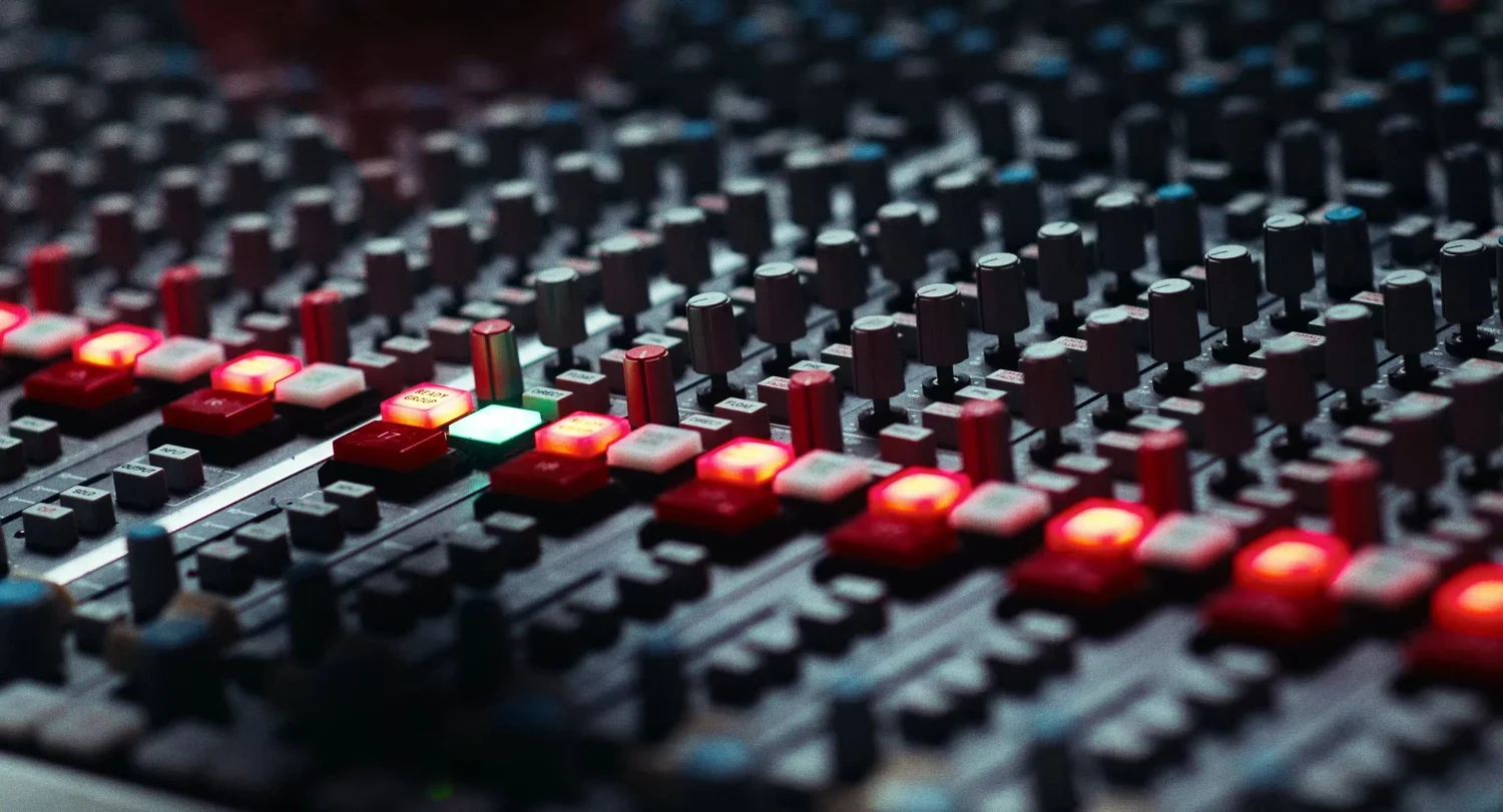 Still from INERTIA: a mixing console with rows of dark knobs and glowing red and green buttons.